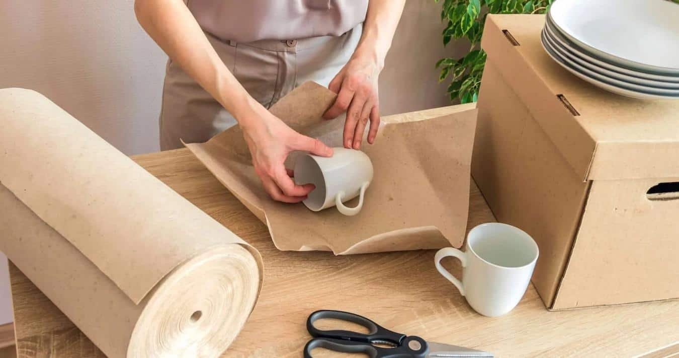 someone packing a mug by wrapping it in packing paper full value protection sharp edges few layers pack items next dish added protection upright position excess space fragile materials pack dishes box pack box